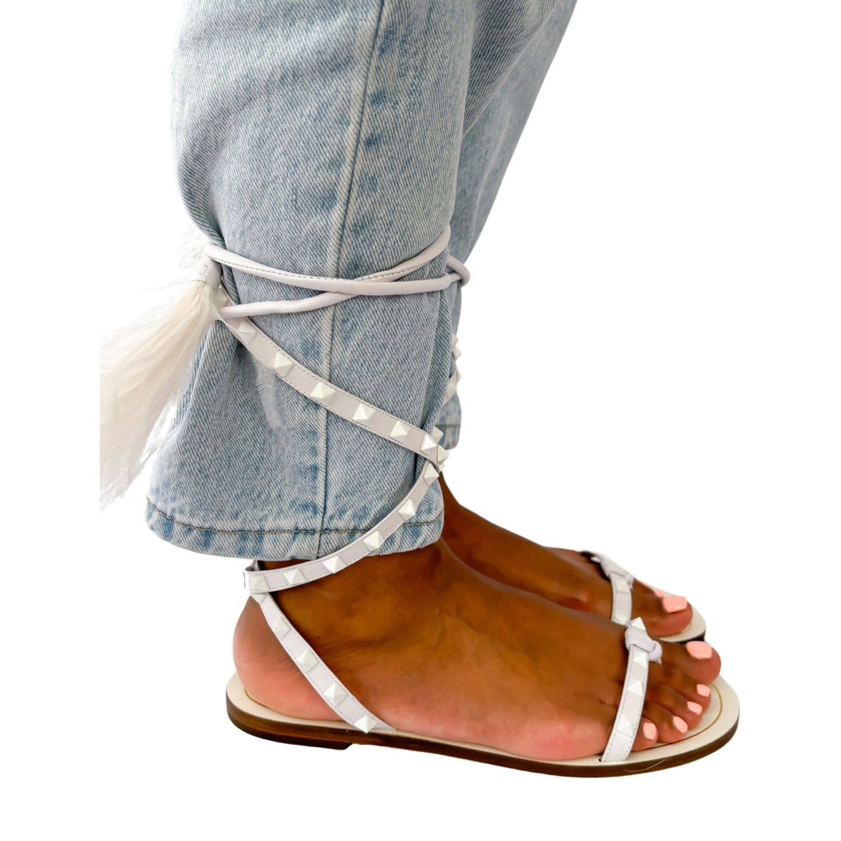 On-foot view of white Valentino Garavani Flair Rockstud lace-up flat sandals styled with jeans.
