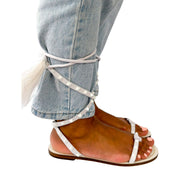 On-foot view of white Valentino Garavani Flair Rockstud lace-up flat sandals styled with jeans.
