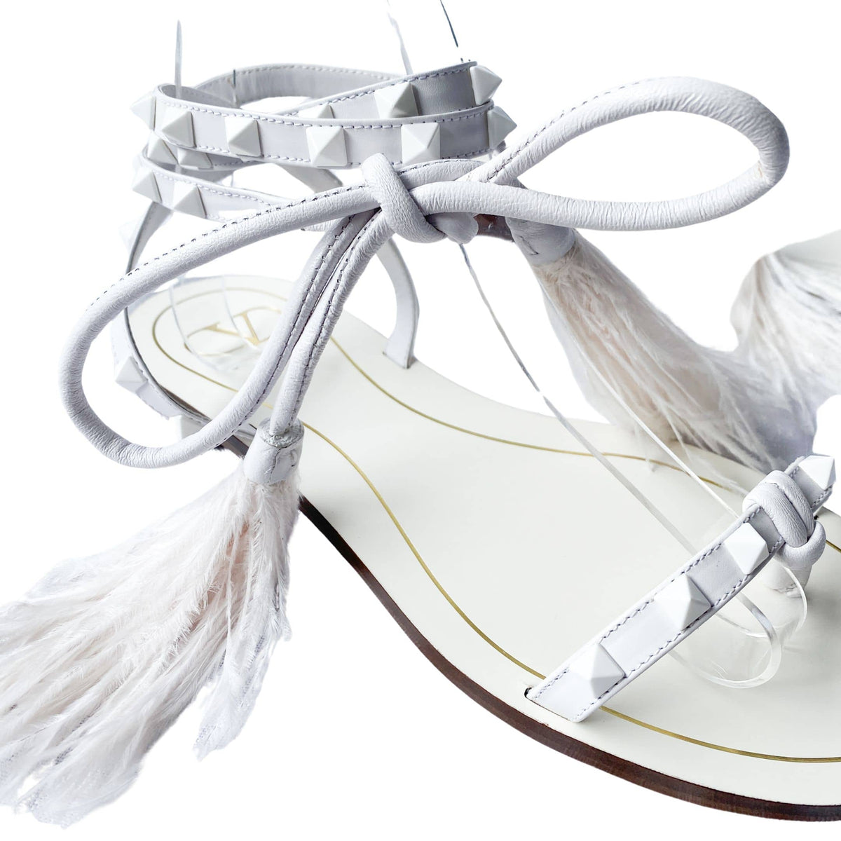 Close-up view of Valentino Garavani Flair white leather sandal detailing the delicate lace-up ties, studs, and feather accents.