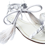 Close-up view of Valentino Garavani Flair white leather sandal detailing the delicate lace-up ties, studs, and feather accents.