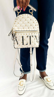Model holding the white Valentino Rockstud backpack by the top handle in a lifestyle setting.
