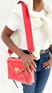 Model wearing the red Valentino Rockstud shoulder bag crossbody styled with a white top and blue jeans.