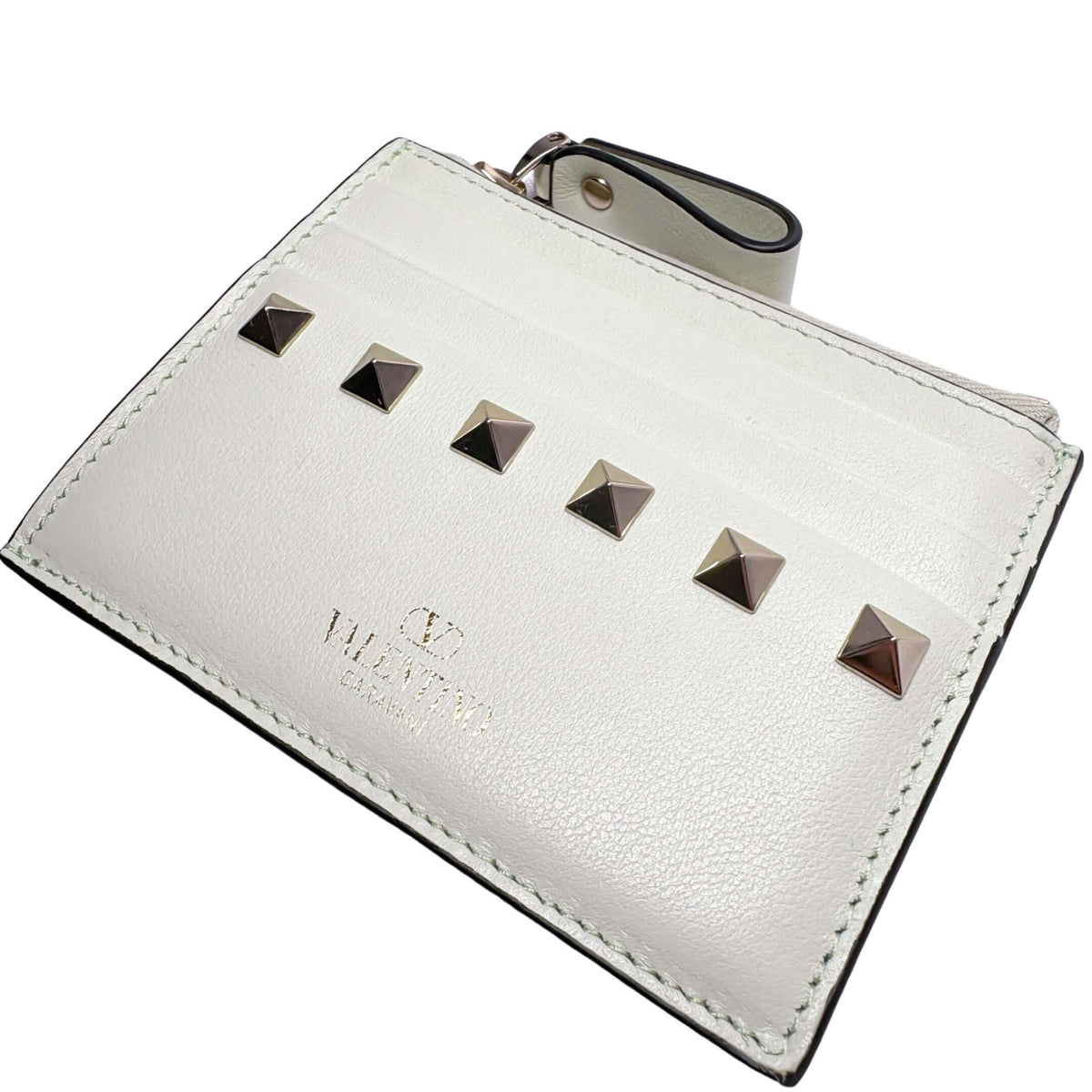 Flat angled view of the white leather Valentino Rockstud coin pouch, highlighting its sleek rectangular shape and top zipper.
