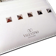 Close-up of the white Valentino card holder, showcasing the gold embossed logo and polished rockstud embellishments.