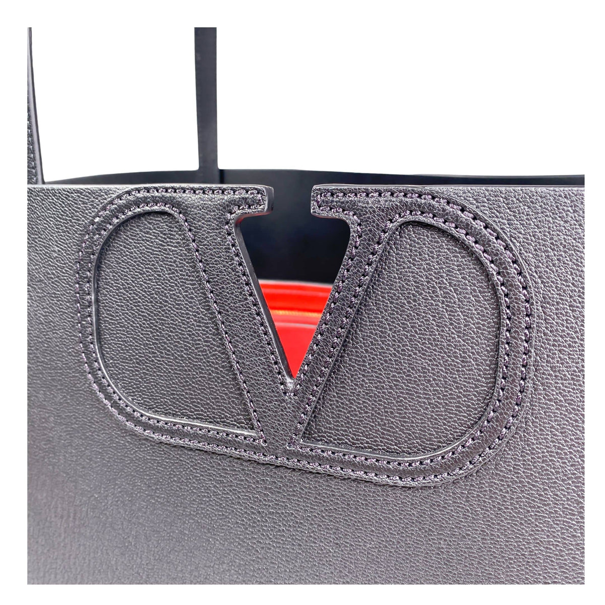 Close-up view of the black leather covered V-logo hardware with vibrant red accent backing on the Valentino tote.