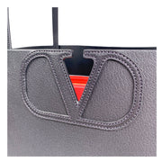 Close-up view of the black leather covered V-logo hardware with vibrant red accent backing on the Valentino tote.