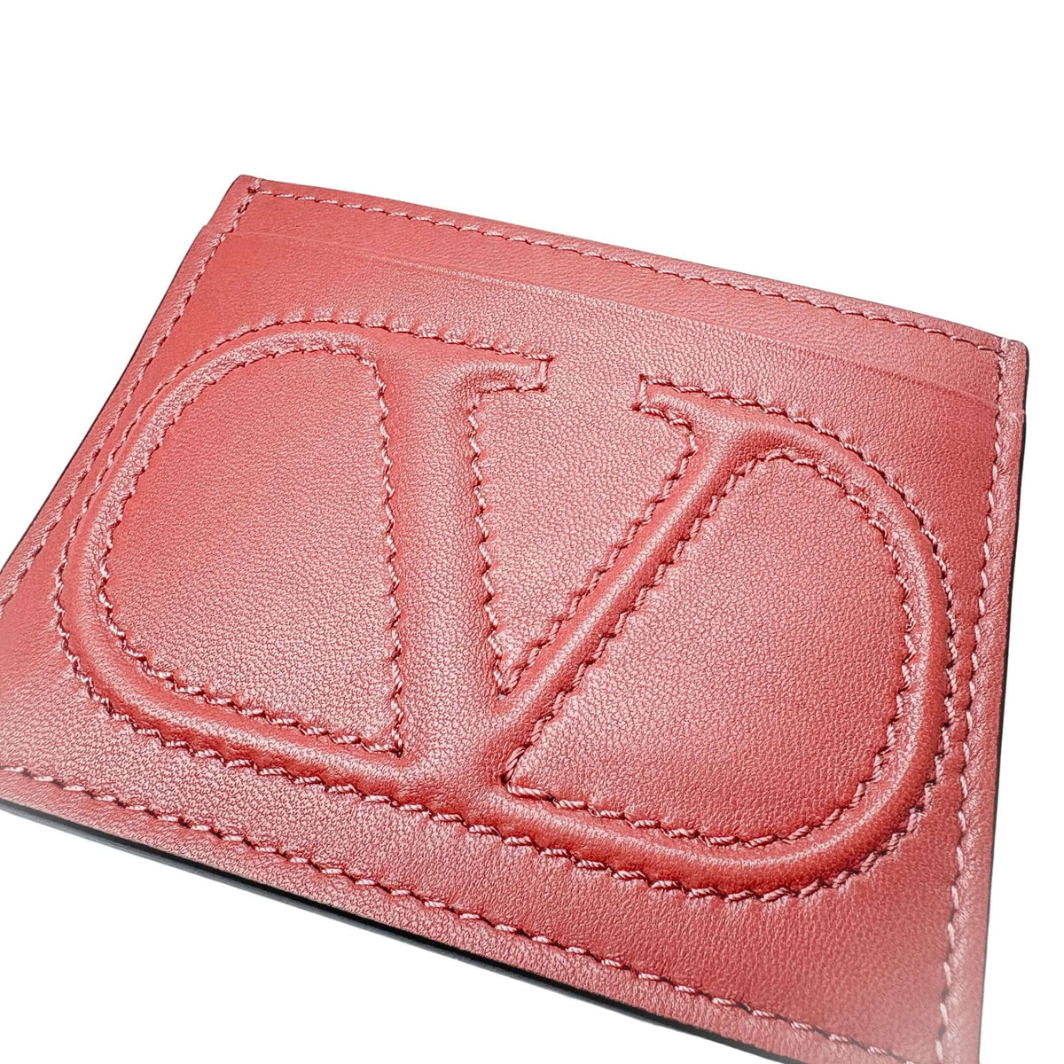 Angled close-up of the red Valentino V-Logo card holder, showcasing the leather texture and precise tonal stitching.