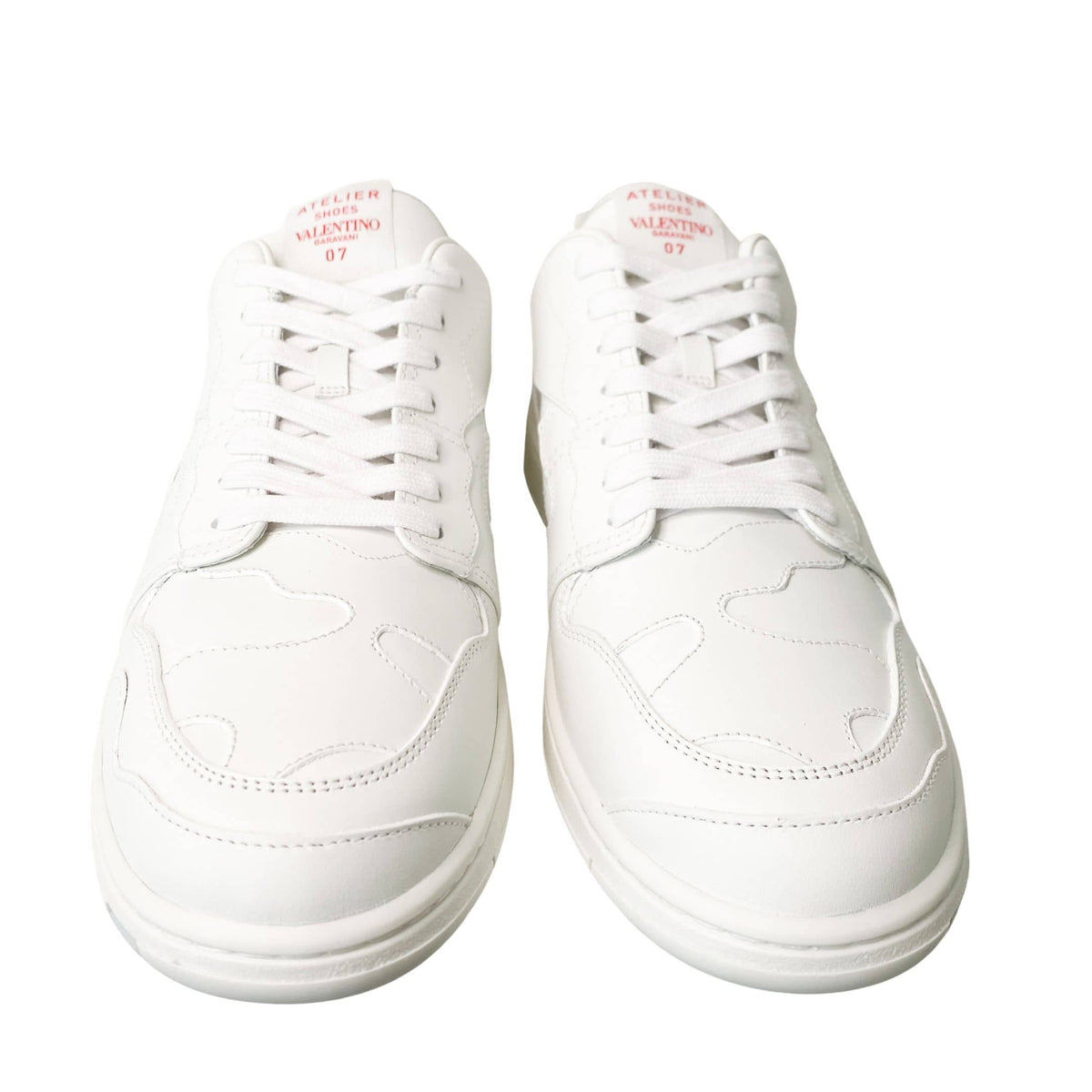 Frontal overhead view of white Valentino Garavani low-top sneakers on a white background.