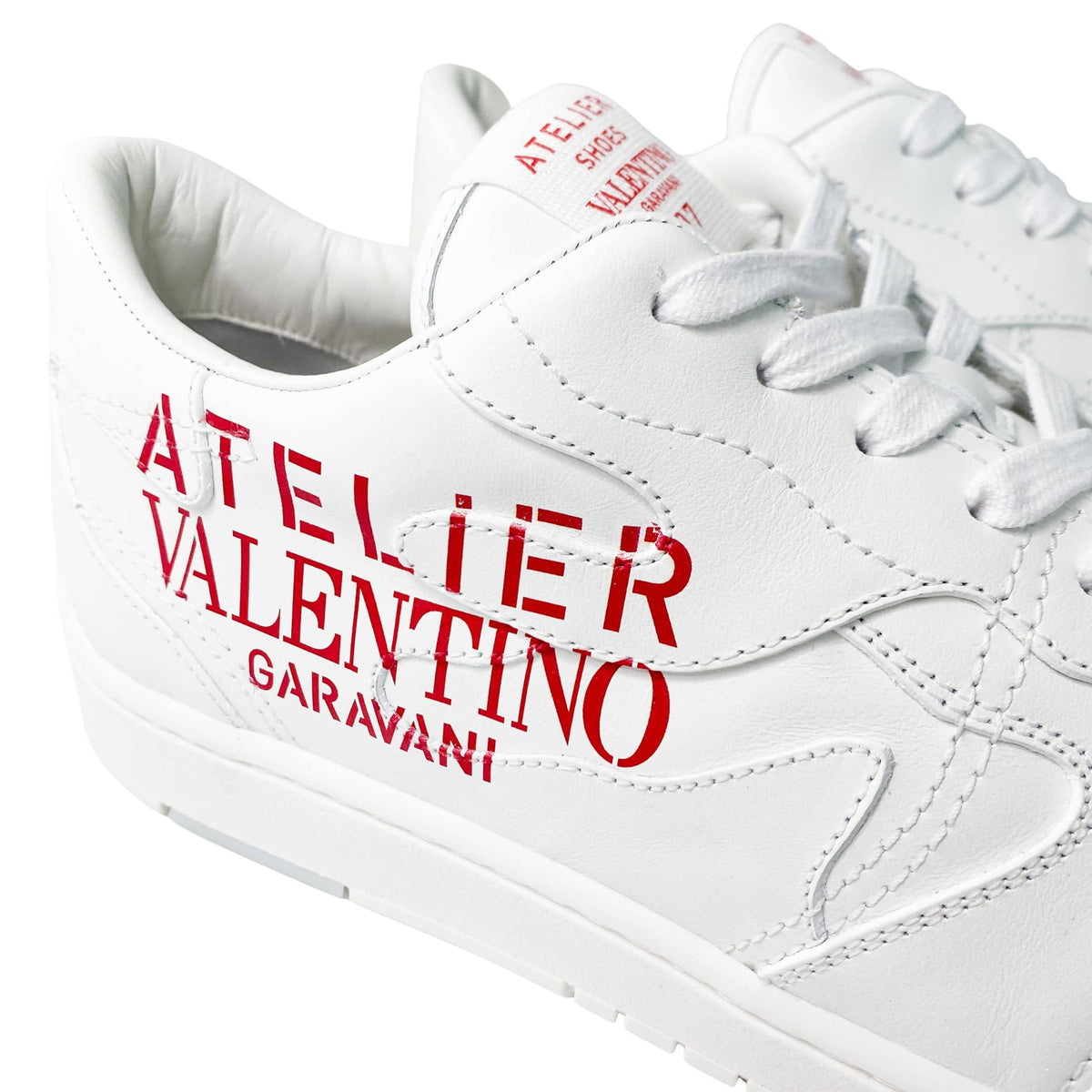 Close-up view of red Atelier Valentino Garavani text print on the side of white leather sneakers.