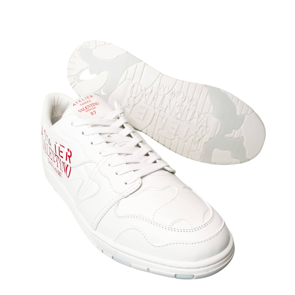 Low-angle perspective view of white Valentino Atelier leather sneakers resting side-by-side.