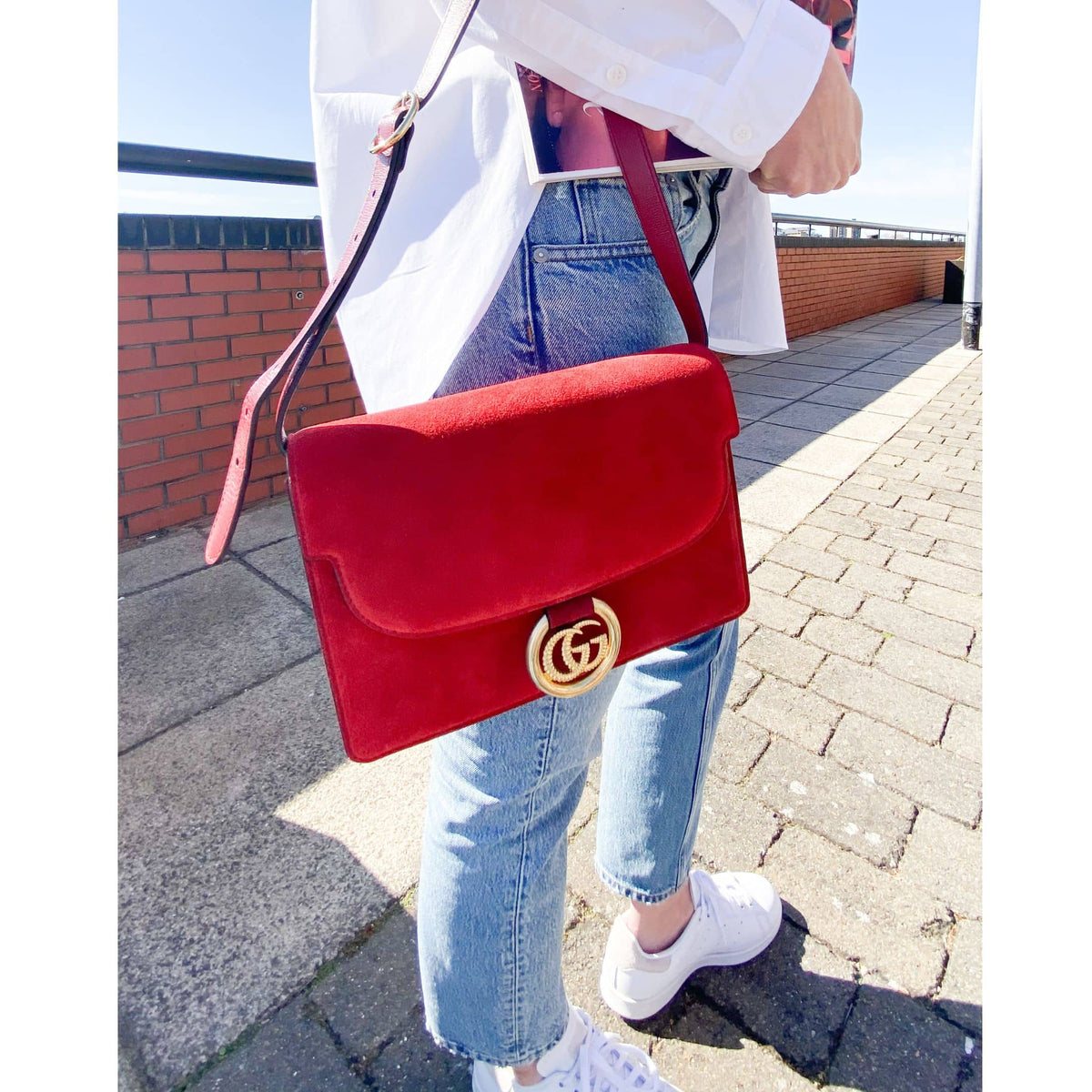 Street style view of a model wearing the red Gucci GG Ring suede shoulder bag, showcasing its size and casual styling.