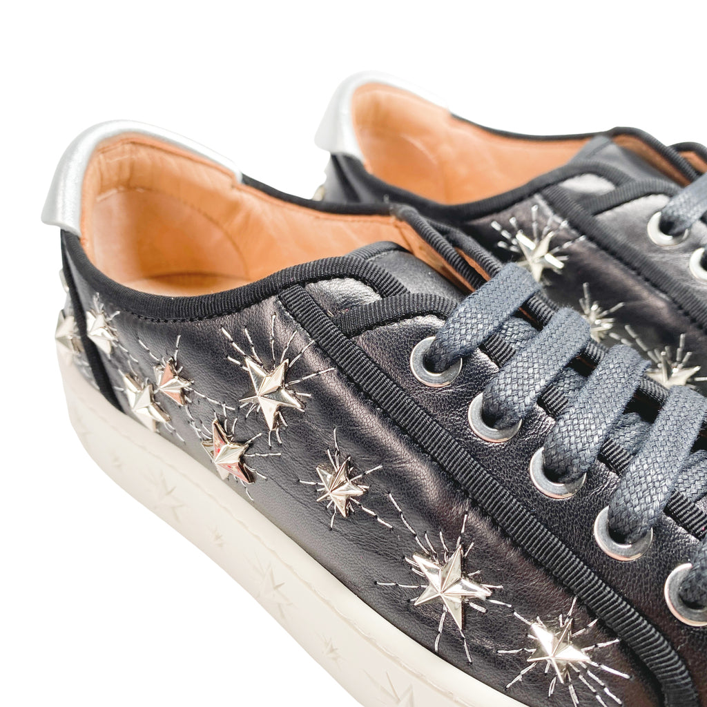 Side profile of Aquazzura Cosmic Star low-top sneakers in black leather, featuring metallic star studs on the upper and embossed star patterns on the white platform sole.
