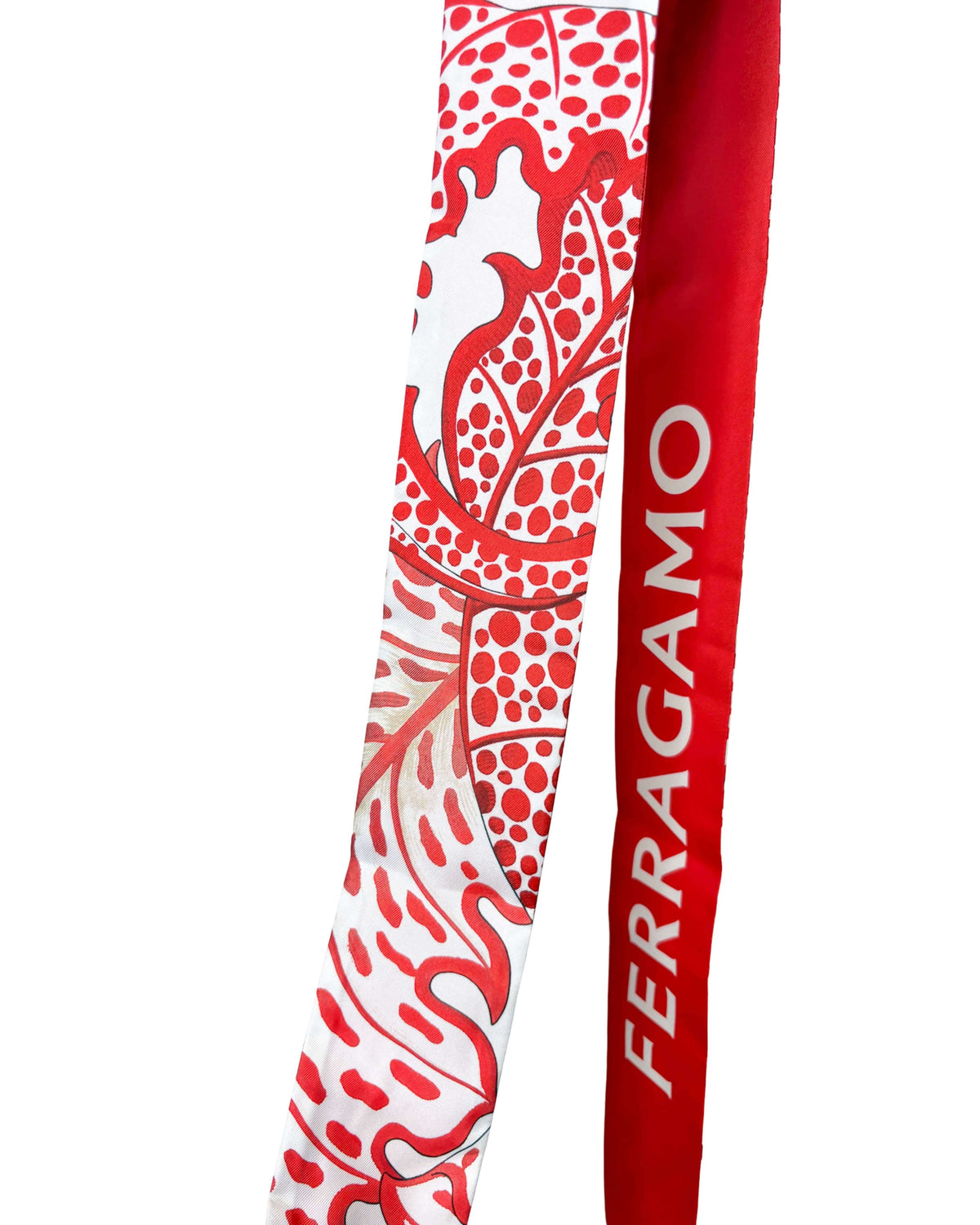 Close-up view of the Salvatore Ferragamo red silk scarf displaying the bold white logo lettering and botanical foliage print.