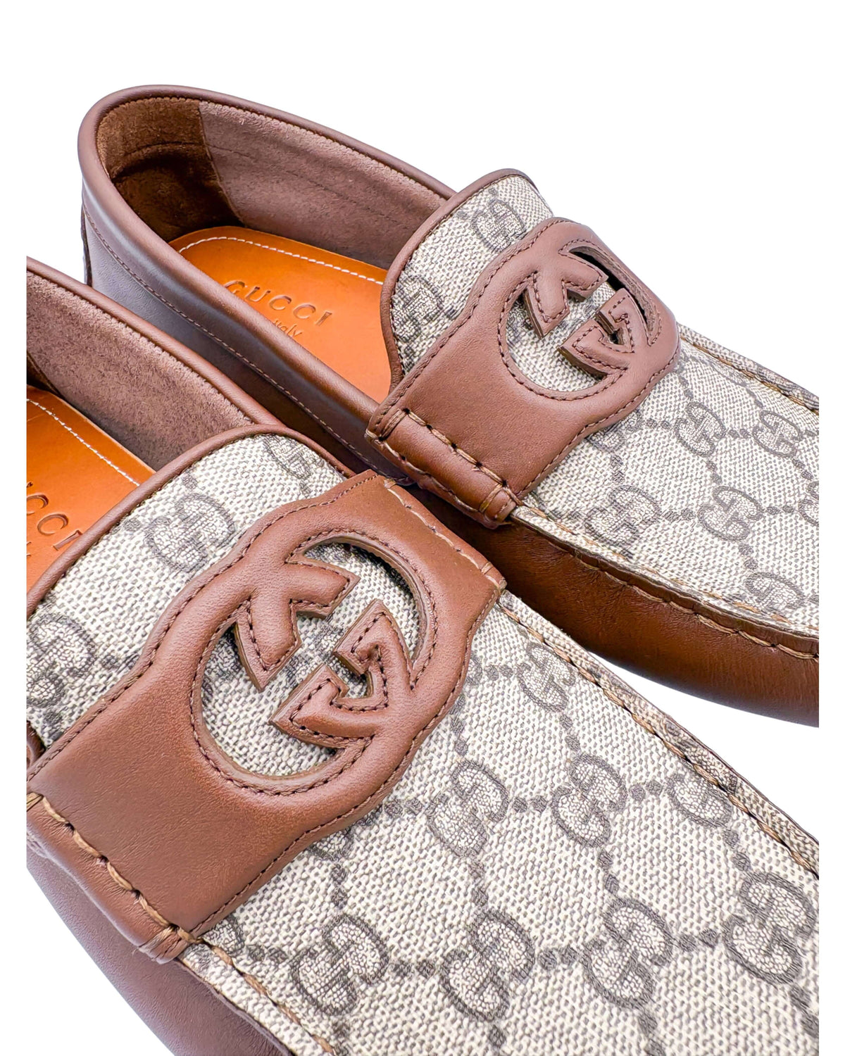 Close-up view of GG Supreme canvas and brown leather strap with interlocking GG logo on Gucci driver loafer.