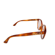 Angled side profile of Gucci light brown sunglasses highlighting the sparkling crystal Gucci logo on the temple arm