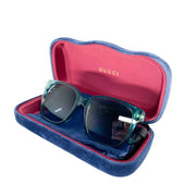 Gucci turquoise sunglasses displayed alongside their signature jewel-toned velvet hard case, satin pouch, and cleaning cloth.