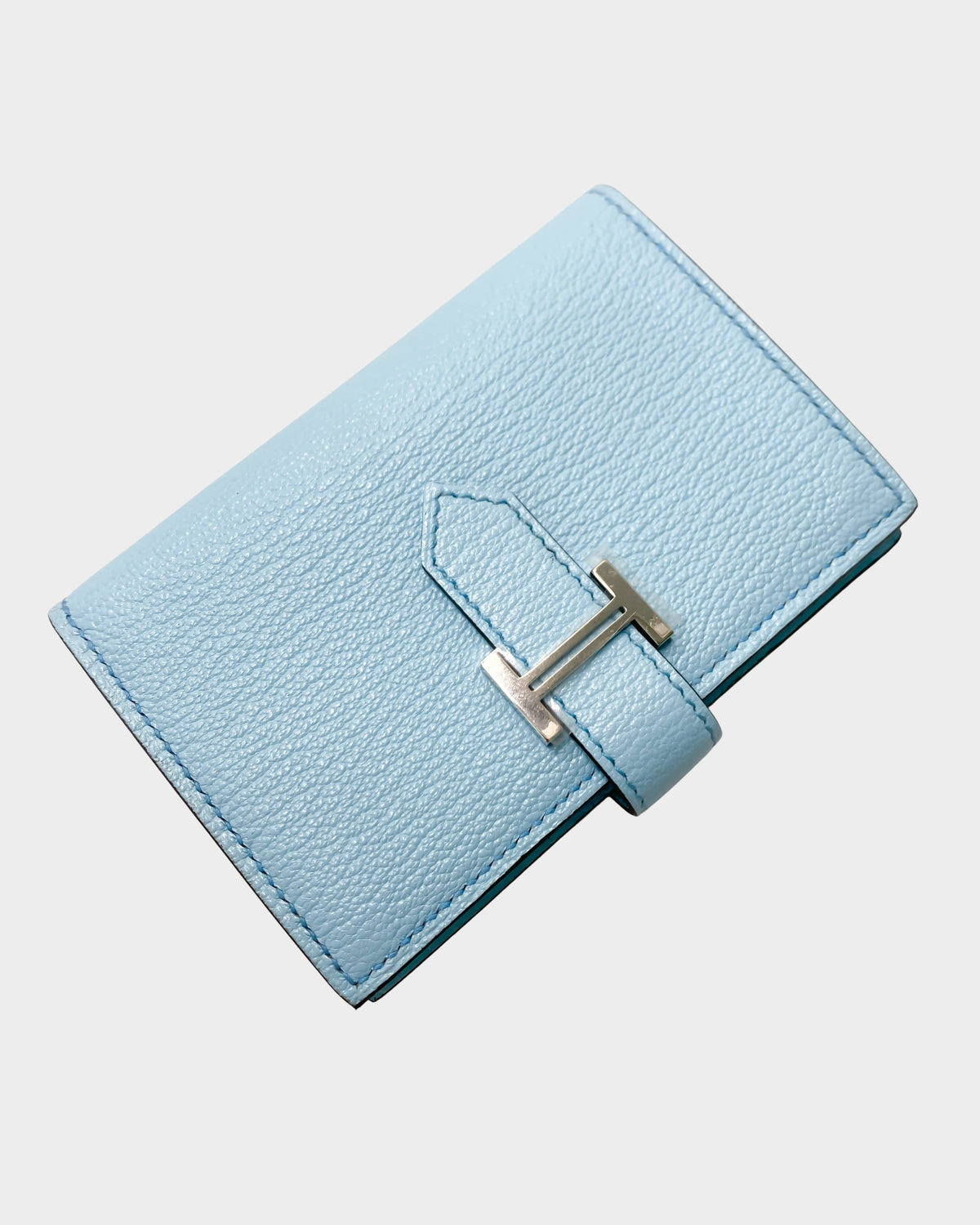 Hermès Bearn Small Wallet in Blue Zephyr leather featuring the signature metallic H tab leather strap closure.