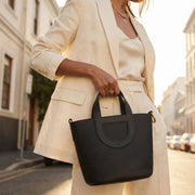 Model wearing Hermès In-the-Loop 18 black Clemence leather top handle bag styled with neutral outfit.