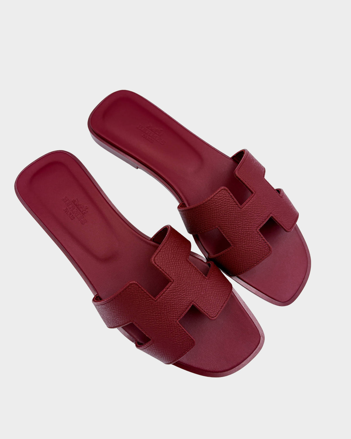 Pair of Hermès Oran sandals in Framboise pink leather featuring the signature H cut-out strap design.