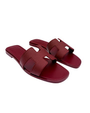 Three-quarter view of Hermès Oran flat sandals in Framboise leather displaying the iconic H vamp design.