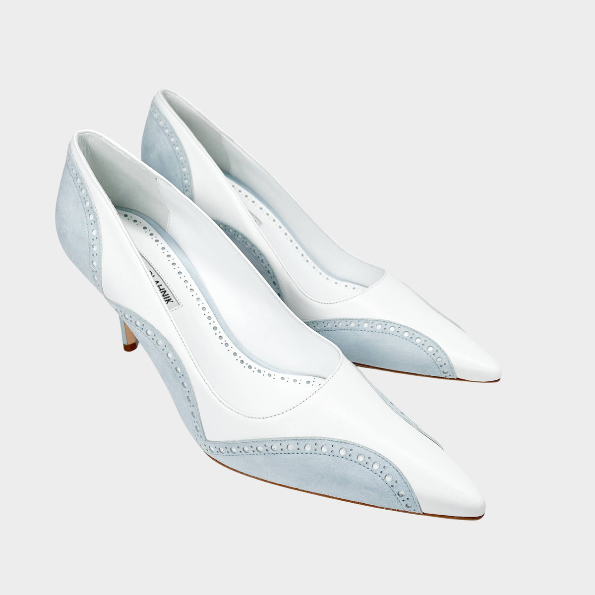 Three-quarter studio view of Manolo Blahnik Minisia 70 white leather pointed-toe pumps featuring light blue lace-trimmed overlays and mid heel.
