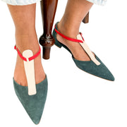 On-foot view of green suede Manolo Blahnik Vree pointed flats with pink T-strap buckle details styled with trousers.