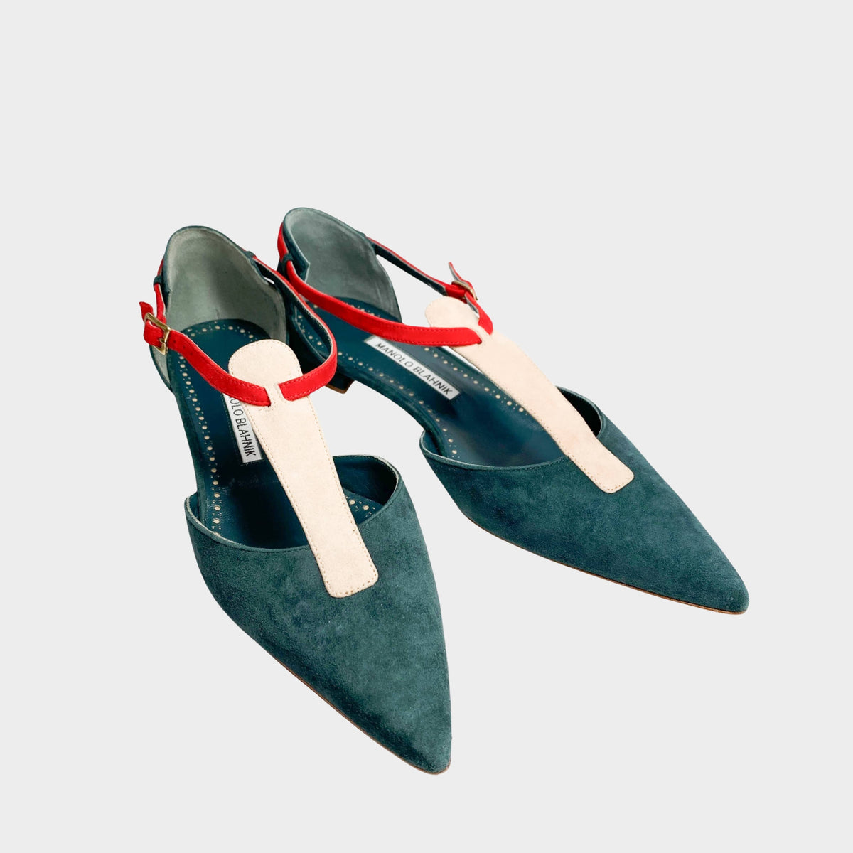 Three-quarter studio view of Manolo Blahnik Vree green suede pointed-toe flats featuring contrasting pink leather T-bar ankle straps.