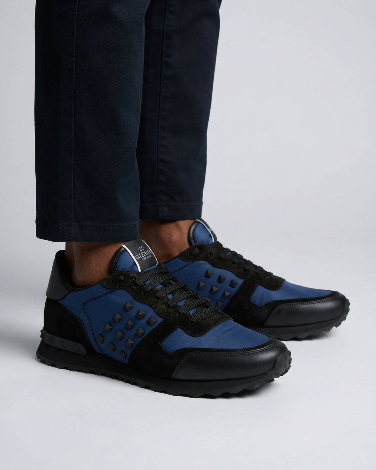 Model wearing Valentino navy blue Rockrunner leather and suede trainers styled with dark trousers.