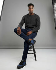 Full-length model view wearing navy Valentino Rockrunner sneakers seated in a grey studio setting.